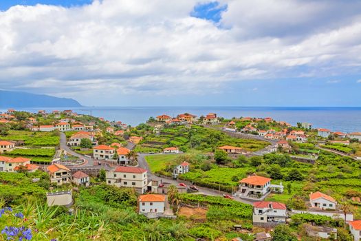 Ponta Delgada, Madeira - June 7, 2013: View over town Ponta Delgada, north coast of Madeira - typical small houses with orange roofs in green nature - the Atlantic Ocean in the background.