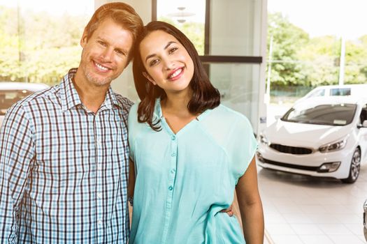 Portrait of happy couple standing against view of row new car 