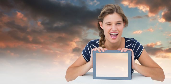Woman showing tablet pc  against blue and orange sky with clouds