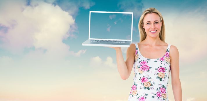 Smiling blonde holding laptop and posing against blue sky with white clouds