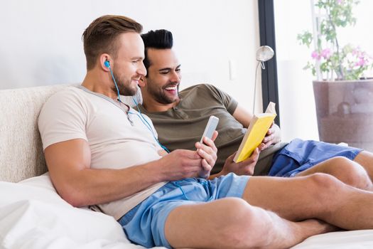 Happy gay couple reading book on bed 