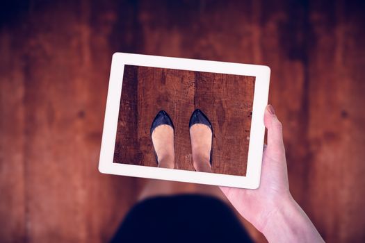 Feminine hand holding tablet against weathered oak floor boards background