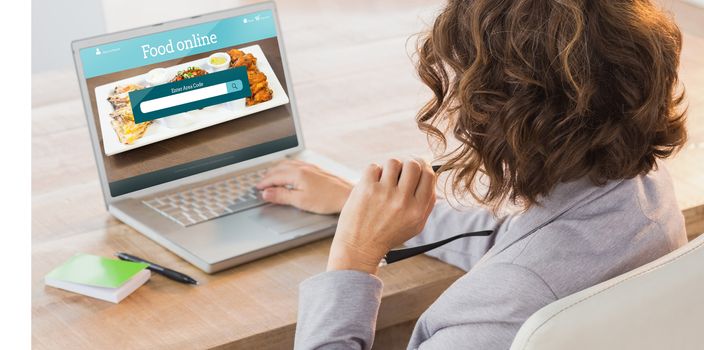 Businesswoman using laptop at desk in creative office against food app