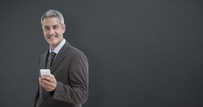 Portrait of smiling businessman holding mobile phone against grey background