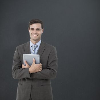 Portrait of smiling businessman holding digital tablet against grey background