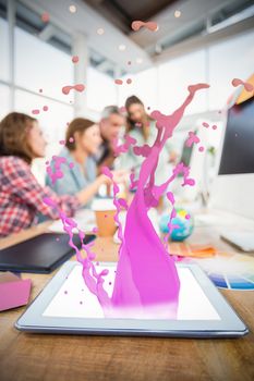 Pink paint splashes and drops against tablet in the foreground with business people in the background 