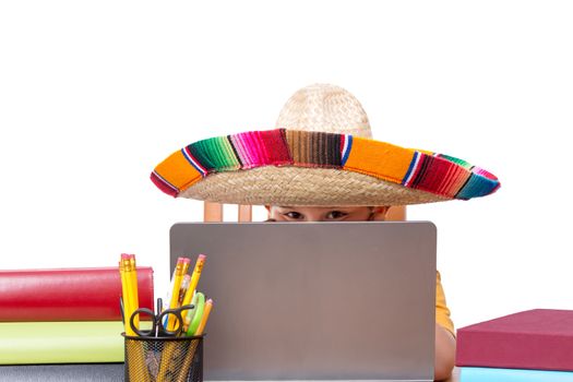 Partially hidden face of child in large colorful sombrero with laptop surrounded by books and pencils over white background