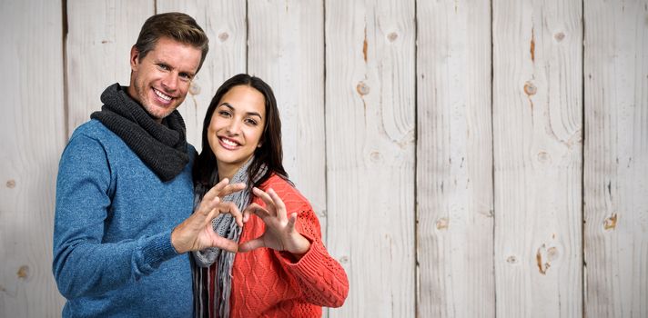 Portrait of couple making heart shape with hands against wooden background