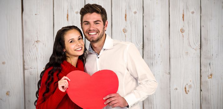 Happy couple holding paper heart against wooden background