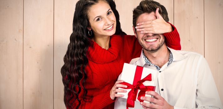 Young woman covering eyes of partner holding gift against wooden planks