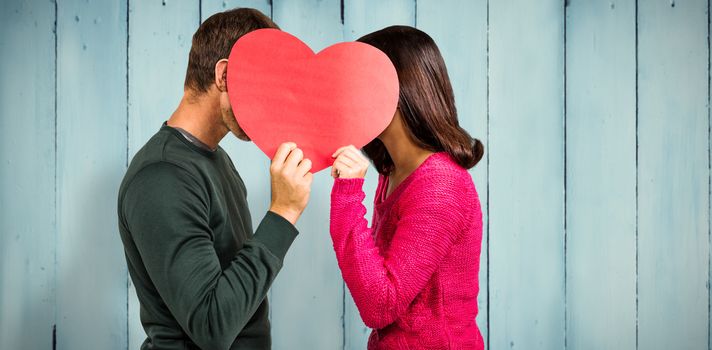 Couple covering faces with heart shape  against wooden planks