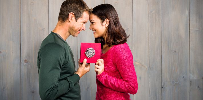 Cheerful couple holding gift box against pale grey wooden planks