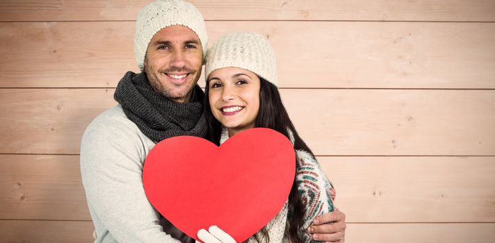 Smiling couple holding paper heart against overhead of wooden planks