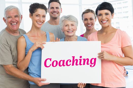 The word coaching and fit people holding blank board in yoga class against grey wall