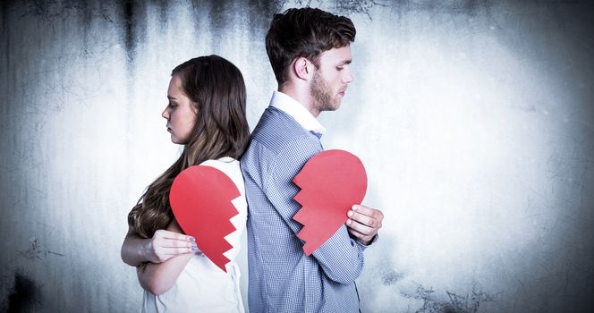 Side view of young couple holding broken heart against grey background