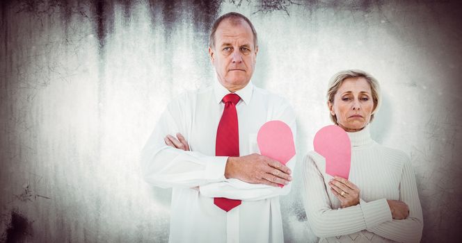 Older couple standing holding broken pink heart against grey background