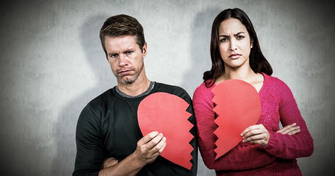 Portrait of serious couple holding cracked heart shape  against white background