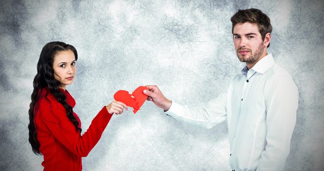 Portrait of couple holding red cracked heart shape  against grey background