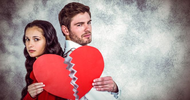 Couple back to back holding heart halves against grey background