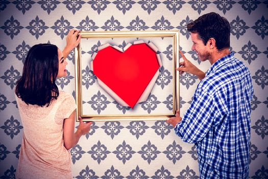 Happy couple holding picture frame against white paper cut in heart shape