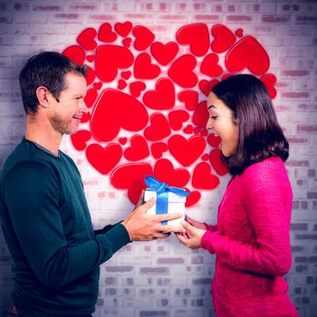 Excited girlfriend taking gift from boyfriend  against grey brick wall