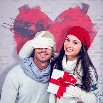 Smiling woman covering partners eyes and holding gift against open door on brick lined wall