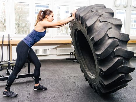 Photo of an attractive young woman working out with a tractor tire at a crossfit gym.
