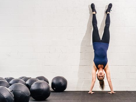Photo of a young fit woman doing a handstand exercise at a crossfit gym.
