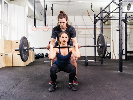 Photo of a young woman at a crossfit gym doing squats while her instructor watches from behind.