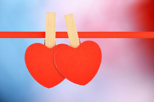 Valentine day love template, two red wooden hearts with clothes pins on textile ribbon on multicolor background 