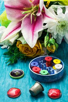 sewing accessories with a bouquet of fresh flowers on turquoise background