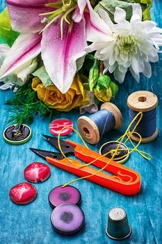 sewing accessories with a bouquet of fresh flowers on turquoise background