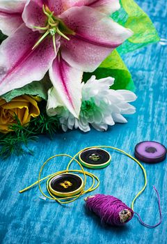 sewing accessories with a bouquet of fresh flowers on turquoise background