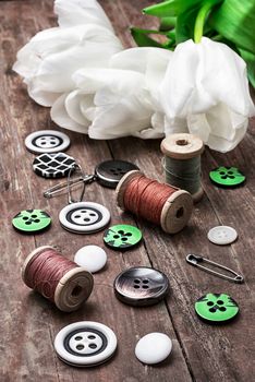 set of sewing accessories from threads and buttons on the background of white tulips