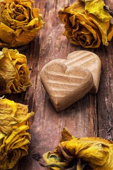 hand-carved symbolic wooden heart on a background of yellow roses