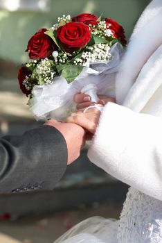 A bride and a groom with bouquet holding hands on the wedding day.