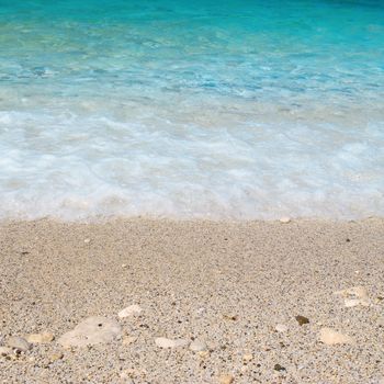 Tropical sand beach with sea waves and stones.