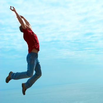 Jumping man against sea with blue sky and clouds