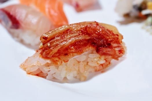 A single piece of Korean style sushi nigiri with kimchi topping on a white plate