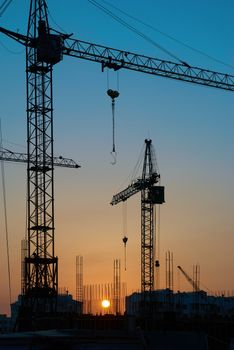 Industrial landscape with silhouettes of cranes on the sunset background