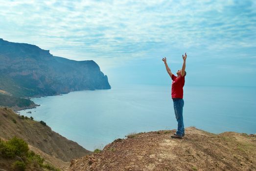 Happy man standing on the cliff with hands up looking at the sea