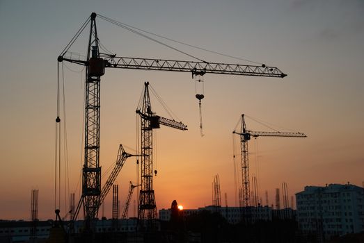 Industrial landscape with silhouettes of cranes on the sunset background