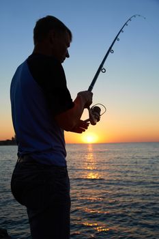 Fisherman fishes on the lake. Silhouette at sunset