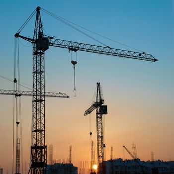 Industrial landscape with silhouettes of cranes on the sunset background