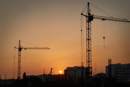 Industrial landscape with silhouettes of cranes on the sunset background