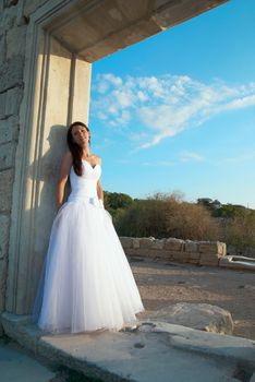 Portrait of beautiful bride in white dress near the old wall.