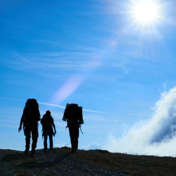 Silhouette of hiking friends against sun and blue sky