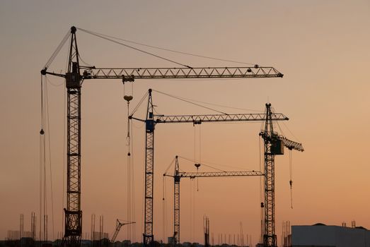 Industrial landscape with silhouettes of cranes on the sunset background