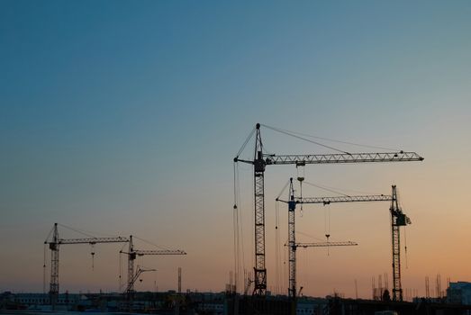 Industrial landscape with silhouettes of cranes on the sunset background