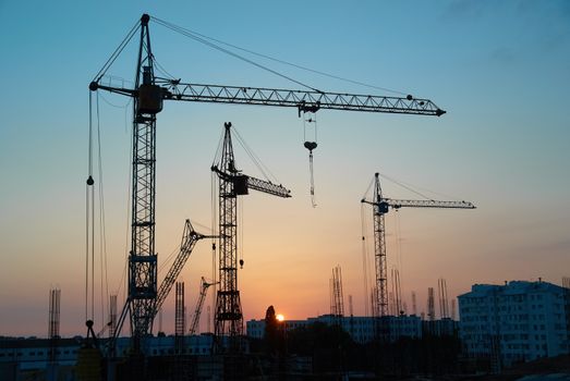 Industrial landscape with silhouettes of cranes on the sunset background